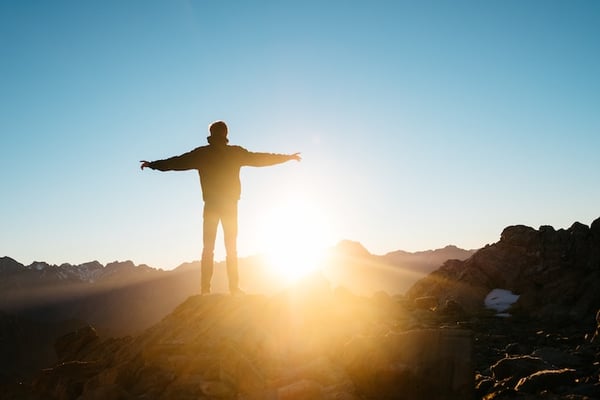 man standing on mountaintop with arms outstretched