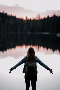 woman standing at a lake with arms stretched open
